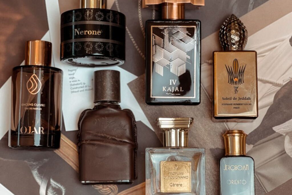 Flaconi profumi colori caldi marrone oro posati su tavolo. Quali sono i migliori profumi d'autunno di nicchia da scoprire? Lasciamoci avvolgere da ambra, vaniglia, legni e muschi enigmatici.
