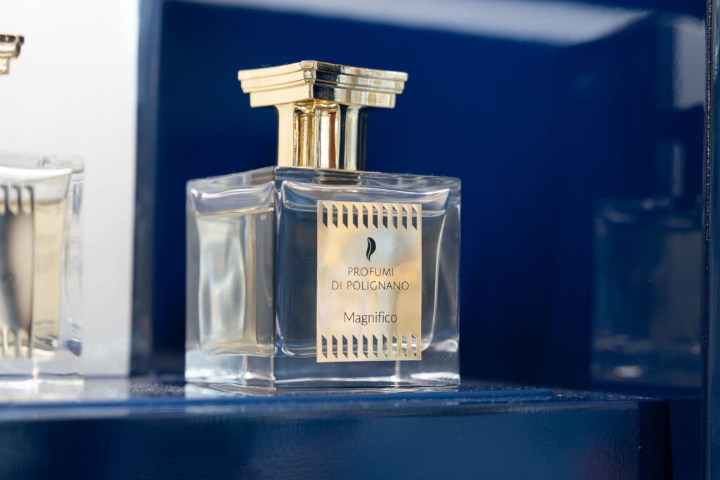 flacone profumo, profumi di polignano profumo, magnifico profumi di polignano, flacone trasparente tappo d'oro, sfondo blu,