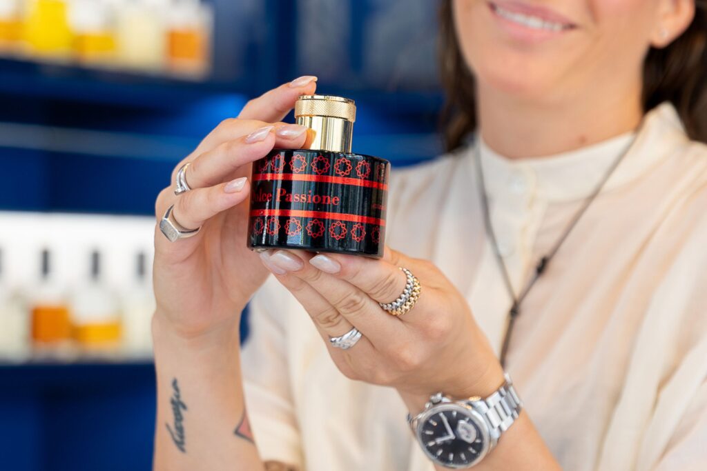 profumi afrodisiaci, profumi per conquistare, feromoni, profumo, profumi, flacone profumo, profumeria, donna, mano, donna tiene profumo, flacone nero,
